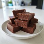 A stack of rich, dark chocolate fudge squares piled high on a white plate.
