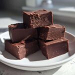 A stack of five rich, dark chocolate fudge squares resting on a small white plate.