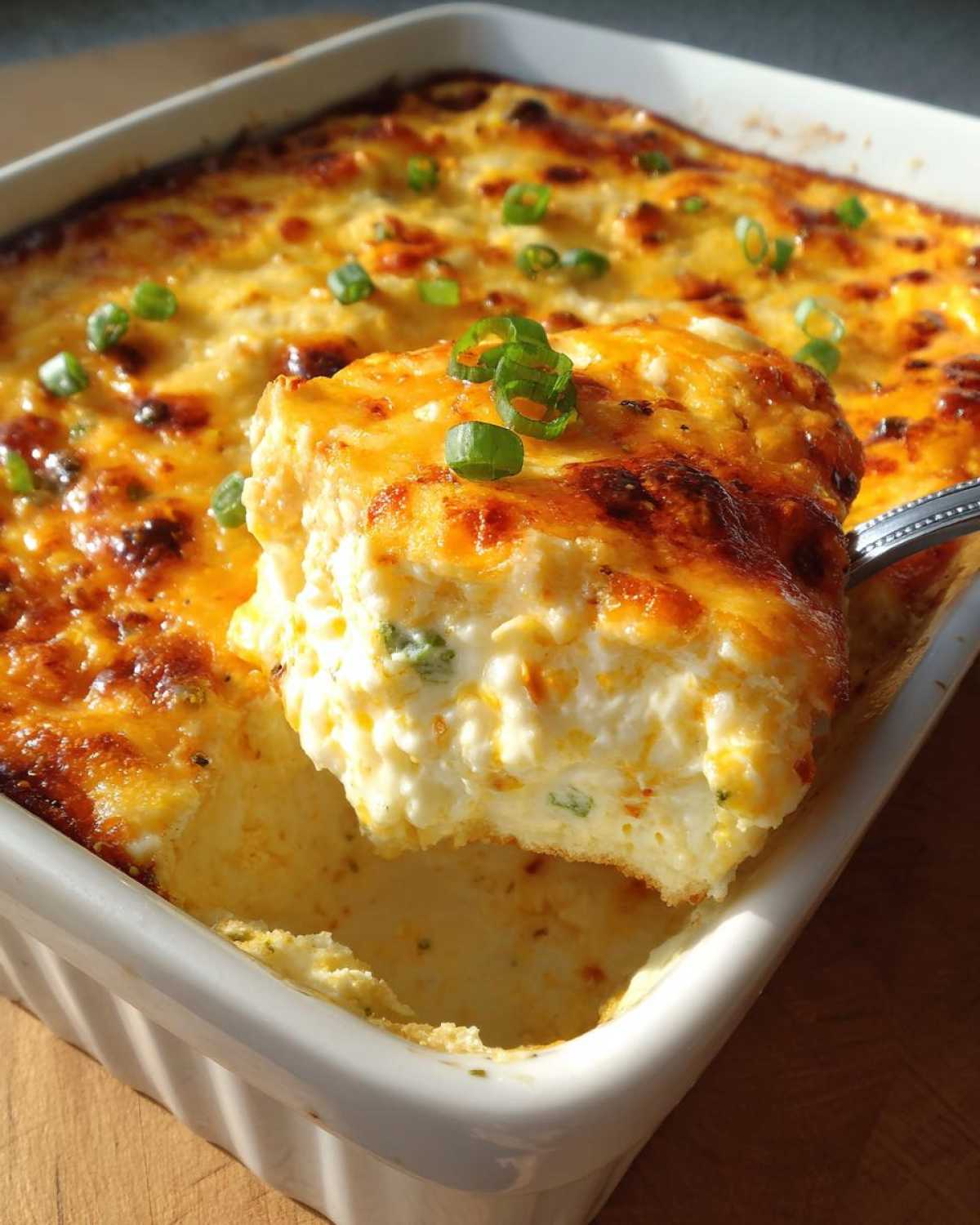 A spoonful of creamy, baked popper dip being lifted from a white baking dish, topped with melted cheese and green onions.
