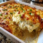 A spoonful of creamy, baked popper dip being lifted from a white casserole dish, showing a golden-brown cheesy top and green onions.