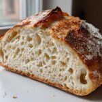 Close-up of the open crumb structure of a freshly baked loaf of bread with a golden crust.