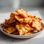 A close-up shot of a small white plate piled high with golden, crispy, homemade cheese crackers.