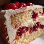 Close-up of a moist slice of cherry cake with white frosting and whole cherries on top.