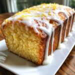 A close-up of a freshly baked lemon pound cake drizzled with white glaze and topped with lemon zest.