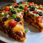 A thick slice of amazing mexican pizza topped with melted cheese, ground beef, black olives, tomatoes, and green onions.
