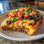 A close-up slice of amazing mexican pizza topped with melted cheese, seasoned beef, tomatoes, olives, and green onions.