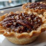 Close-up of a freshly baked mini pecan pie with a gooey, glossy filling and whole pecans on top.