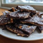 A pile of broken pieces of dark chocolate peanut butter pretzel bark dusted with powdered sugar.