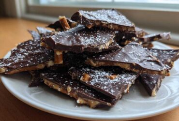 A pile of broken pieces of dark chocolate peanut butter pretzel bark dusted with powdered sugar.