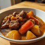Close-up of a white bowl filled with rich, brown pork stew featuring tender meat chunks, carrots, and potatoes.