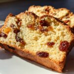 Two thick slices of golden, fluffy raisin bread studded with plump raisins, resting on a white plate.