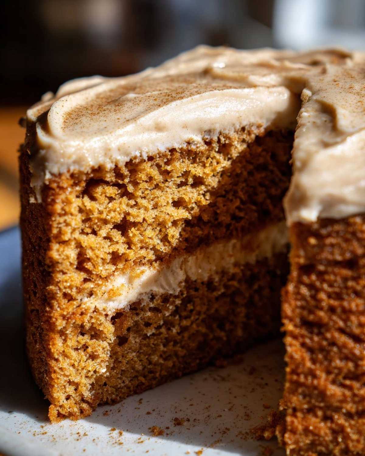 A close-up slice of moist, layered spice cake topped with creamy frosting and a dusting of cinnamon.