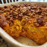 Close-up of a baked sweet potato souffle in a white dish, showing the bright orange interior and crunchy pecan topping.
