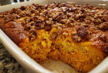 Close-up of a baked sweet potato souffle in a white dish, showing the bright orange interior and crunchy pecan topping.