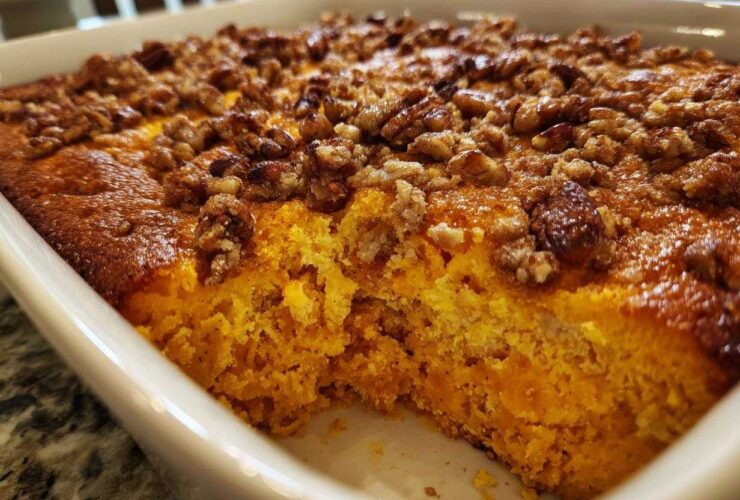 Close-up of a baked sweet potato souffle in a white dish, showing the bright orange interior and crunchy pecan topping.