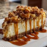 A decadent slice of apple pie cheesecake topped with spiced apples, crumble, and generous caramel drizzle.