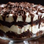 Close-up of a layered Baileys Chocolate Cheesecake Trifle featuring dark cake, white cream, chocolate drizzle, and shavings.