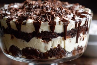 Close-up of a layered Baileys Chocolate Cheesecake Trifle featuring dark cake, white cream, chocolate drizzle, and shavings.