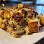 Close-up of a serving of moist sausage stuffing recipe with golden-brown bread cubes and herbs.