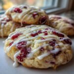 Close-up of chewy cranberry orange cookies topped with white icing drizzle and dried cranberries.