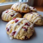 A stack of freshly baked cranberry orange cookies drizzled with white icing, showcasing dried cranberries and orange zest.