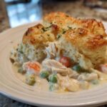 A serving of creamy chicken pot pie casserole topped with golden biscuits and sprinkled with herbs.