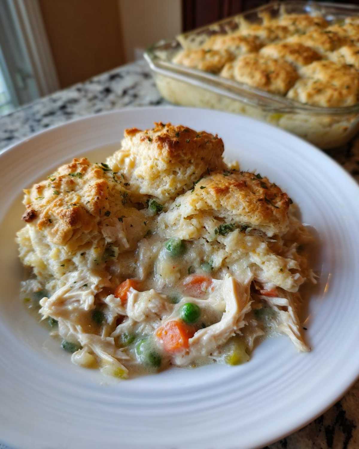 A serving of creamy chicken pot pie casserole topped with golden biscuits on a white plate.