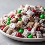 A close-up of homemade christmas puppy chow coated in powdered sugar, mixed with red and green M&M's and pecans.