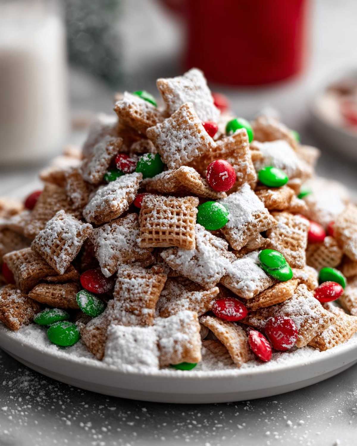 A close-up of a mound of Christmas puppy chow dusted with powdered sugar and mixed with red and green candies.
