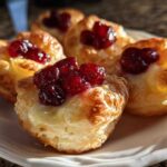 Close-up of golden, flaky pastry cups filled with melted brie and topped with jewel-toned cranberry sauce, showcasing perfect cranberry brie bites.