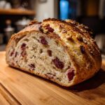 Cross-section view of a rustic cranberry walnut bread loaf showing the open crumb texture, dried cranberries, and walnuts on top.