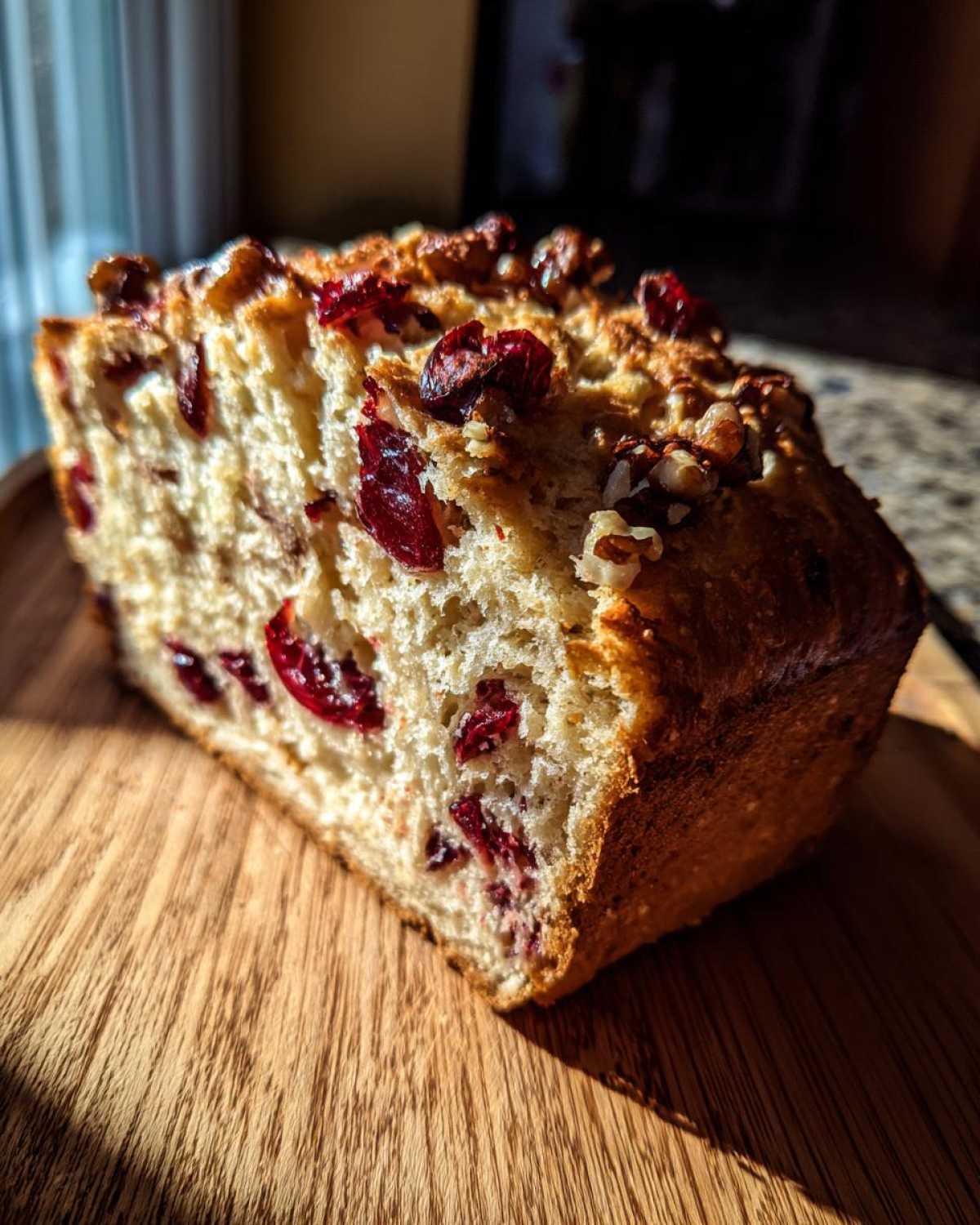 A thick slice of homemade cranberry walnut bread showing bright red dried cranberries and chopped walnuts embedded in the light crumb.