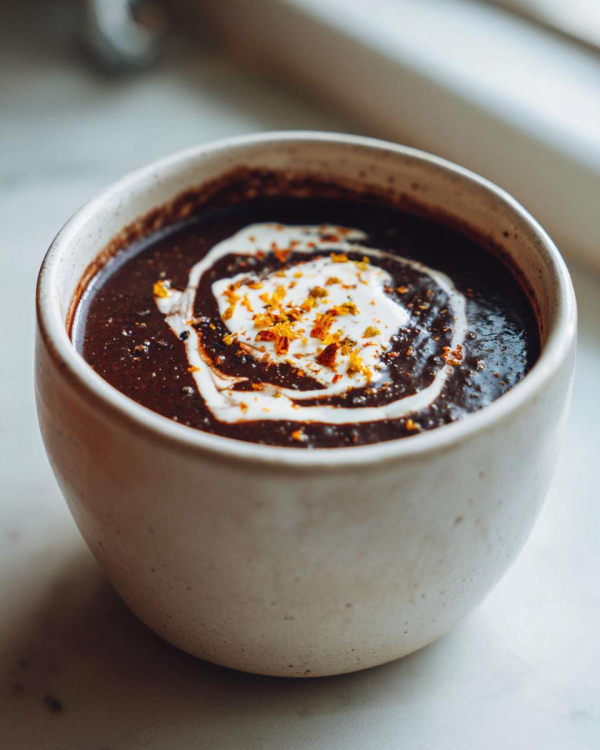 Close-up of creamy black bean soup garnished with a swirl of cream and orange spices.