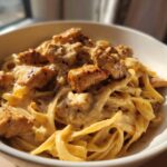 Close-up of creamy chicken pasta featuring fettuccine noodles coated in a rich sauce and topped with seasoned, cubed chicken pieces.