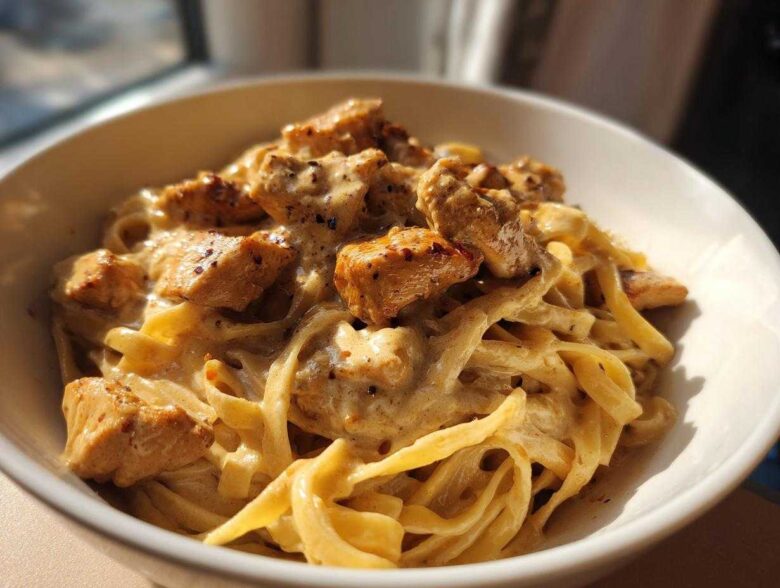Close-up of creamy chicken pasta featuring fettuccine noodles coated in a rich sauce and topped with seasoned, cubed chicken pieces.