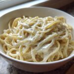 Close-up of fettuccine pasta generously coated in creamy homemade olive garden alfredo sauce and topped with pepper.