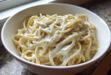 Close-up of fettuccine pasta generously coated in creamy homemade olive garden alfredo sauce and topped with pepper.