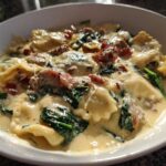 A close-up of a bowl of creamy ravioli soup featuring spinach and bits of bacon, showcasing the rich sauce.