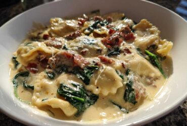 A close-up of a bowl of creamy ravioli soup featuring spinach and bits of bacon, showcasing the rich sauce.