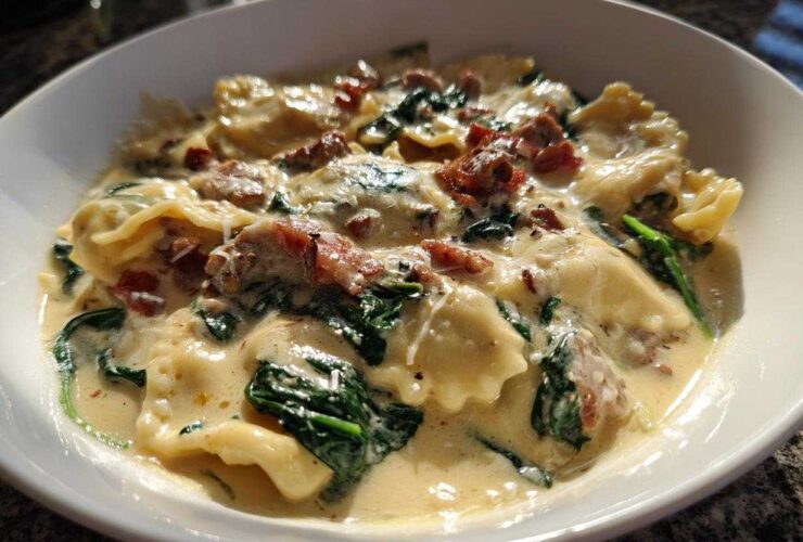 A close-up of a bowl of creamy ravioli soup featuring spinach and bits of bacon, showcasing the rich sauce.