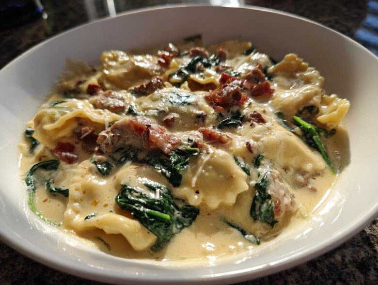 A close-up of a bowl of creamy ravioli soup featuring spinach and bits of bacon, showcasing the rich sauce.