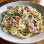 Close-up of creamy shrimp alfredo pasta topped with sautéed shrimp, grated cheese, and fresh parsley.