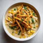 Overhead view of a bowl of creamy tortilla soup loaded with shredded chicken, corn, and topped with crispy tortilla strips and cilantro.