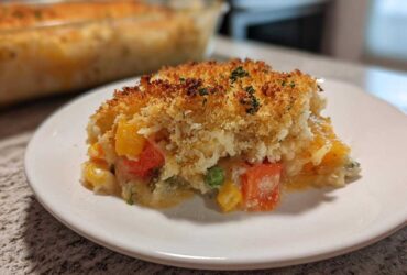 A serving of creamy vegetable casserole with mixed vegetables and a golden, crispy breadcrumb topping.