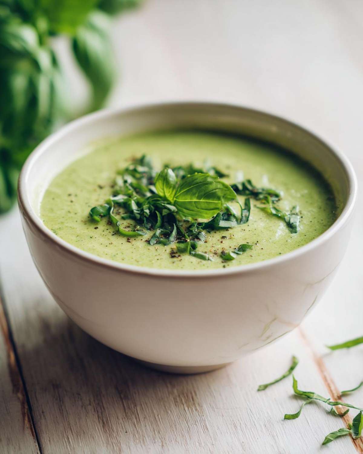 A bowl of creamy green zucchini soup topped with fresh basil chiffonade and black pepper.