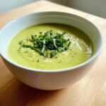 Close-up of a bowl of creamy zucchini soup garnished with fresh chiffonade basil and black pepper.