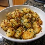 A white bowl filled with golden brown, crispy air fryer gnocchi topped with Parmesan cheese and fresh parsley.