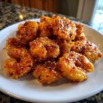Close-up of a pile of crispy, glazed Bang Bang Shrimp seasoned with red pepper flakes on a white plate.
