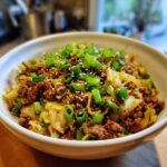 Close-up of a white bowl filled with savory egg roll in a bowl mixture, topped generously with sliced green onions and sesame seeds.