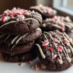 A stack of rich, dark double chocolate peppermint cookies drizzled with white chocolate and topped with crushed candy canes.